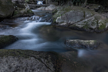 Blurred mountain stream flowing over dark granite boulders through rainforest, Samui, Thailand