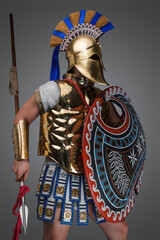 Portrait of warrior from ancient greece dressed in armor and helmet holding shield and spear.