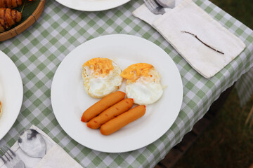 Breakfast on the table. Asian couple cooking food fried egg and bread with sausage at camp.