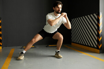 Man athlete training hard at gym, stretching and warming his body up before doing special exercises for leg muscles before starting crossfit workout, lunging sideward with clenched fists