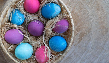 Happy Easter holiday. Bright colored eggs in a nutural basket with hay on a wooden cut natural background. Spring Easter concept in eco style. Top view. Copy space