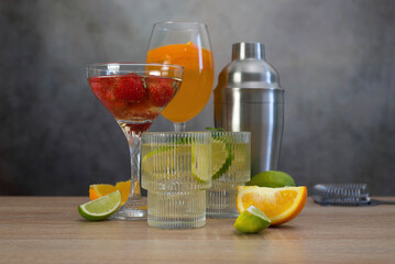 assorted cocktails: two glasses of mojito, orange cocktail, cocktail with strawberries, fruits and shaker on a gray background.