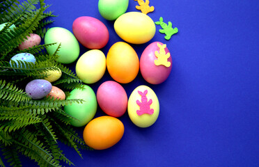 Fototapeta na wymiar Colorful Easter eggs. Banner, wallpaper, postcard, social media post with copy space for text. Painted eggs, located on one side on a dark purple background, green leaves of the plant.