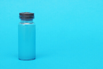 Glass ampoule with blue liquid on a blue background.