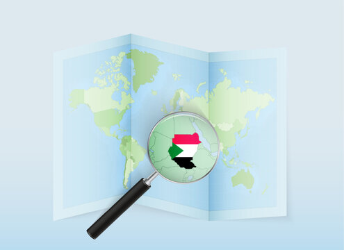 A folded world map with a magnifying lens pointing towards Sudan. Map and flag of Italy in loupe.