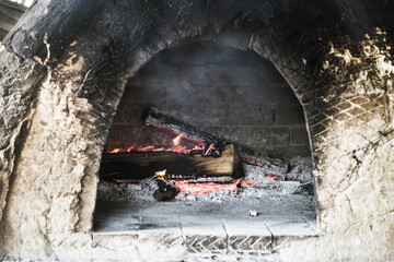 Smoky antique brick oven outdoor with ashes and burning fire inside. The small brick furnace with soot and fire in it. The red flame burns in a brick wall oven. Old rustic bread oven.