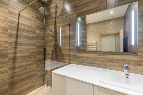 Brown tile shower enclosure with tropical shower head. Faucet with sink and large mirror.