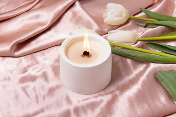 Handmade candle and white tulips on pink silk background. Candle in a concrete candlestick