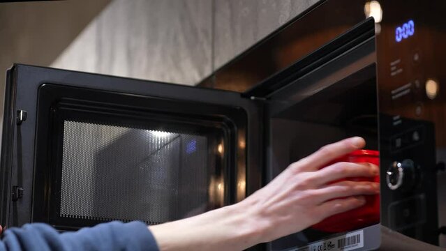 A man puts food in the microwave to heat up. Semi-finished products, fast food. Microwave and male hands close-up