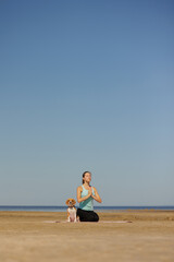 Fototapeta premium woman and dog meditate on yoga mat on ocean in morning. sports outdoor for mental and physical health, breathing and physical practices. taking care of the body, spine and muscles