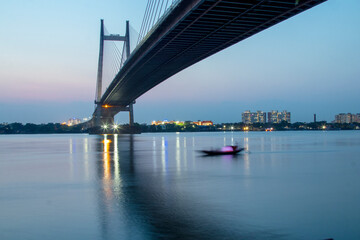 Fototapeta premium Boat in the river Ganges at Kolkata It is a toll bridge over the Hooghly River in West Bengal, India, linking the cities of Kolkata and Howrah.