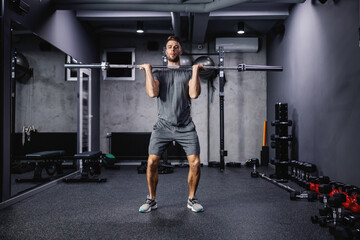 Naklejka na ściany i meble Cross fit training with barbell lifting. An attractive and muscular man. A man in sportswear pumps his arm muscles and lifts a barbell in a modern gym. Copy space for marketing massage