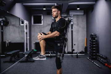 Fototapeta na wymiar Fit man in the electric muscular suit in the training center. A man on individual training wears EMS equipment and stretches muscles at the beginning of training. Electrical muscle stimulation