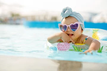Foto op Plexiglas Cute funny toddler girl in colorful swimsuit and sunglasses relaxing on inflatable toy ring floating in pool have fun during summer vacation in tropical resort. Child having fun in swimming pool.  © KDdesignphoto