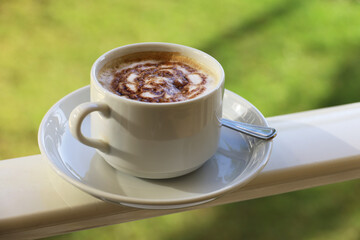 Coffee cup with cappuccino on green park background. Morning mood, chocolate pattern on whipped cream