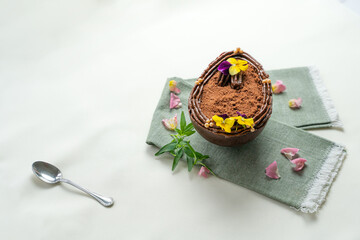 Presentation of an Easter egg from a pastry stuffed with chocolate and caramel, and decorated with showy yellow flowers..