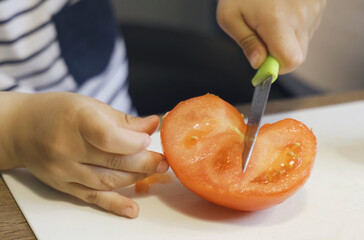 A little boy cuts a tomato with a knife.