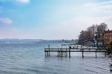 Fototapeta na wymiar Boathouses and jetty in Seeshaupt in Bavaria at Lake Starnberg on a slightly cloudy winter day