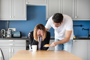 Obraz premium Tired business woman sits at the table and her husband householder takes care about her at home