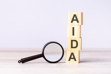 magnifying glass and wooden blocks with text AIDA on wood table, grey background