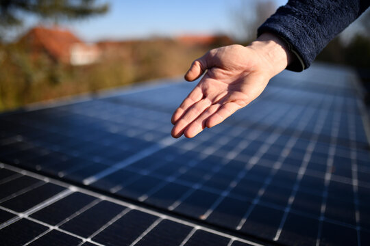 Beste Nahaufnahme der rechten Hand eines Solar Installateurs mit neuen, unscharfen Fotovoltaik Modulen im Hintergrund auf dem Haus Dach