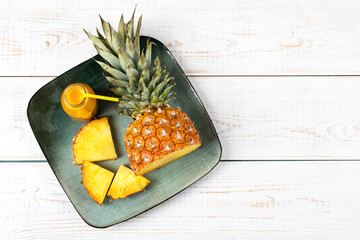 Slices of juicy pineapple and a fresh healthy smoothie in a glass bottle and a straw in a green plate on a wooden background. Healthy, detox and dietary nutrition concept.
