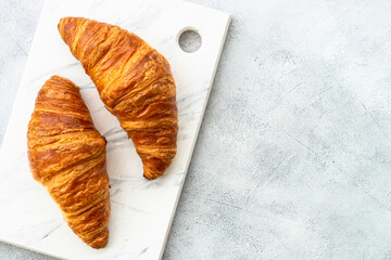 Croissant on cutting board at white table. French bakery, top view.