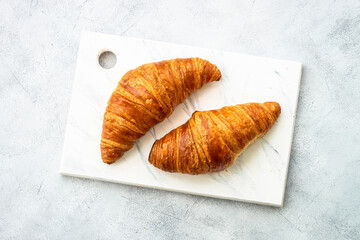 Croissant on cutting board at white table top view. French bakery.