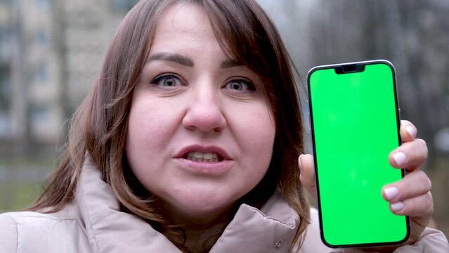 adult woman on the street in the rain with a phone green screen chromakey shows with a kiss how she likes advertising she smiles kisses three fingers and spreads them to the side mmm how cool