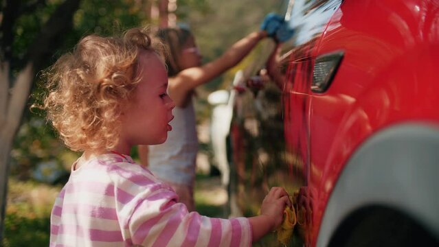 Little girl washes a red car in a garden