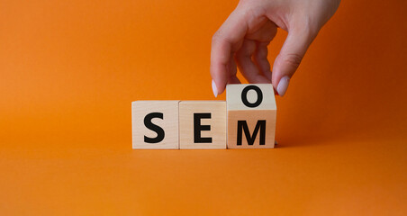 Seo and Sem symbol. Hand turns a cube and changes the word Sem to Seo. Beautiful orange background. Businessman hand. Business and Seo and Sem concept. Copy space