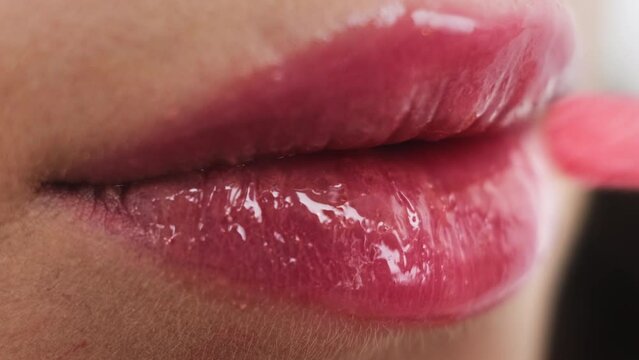 Woman applies bright pink lip gloss using applicator. Female person does professional makeup preparing for graduation party extreme closeup