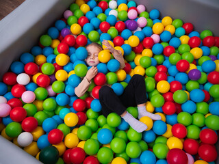 Cute little girl playing on multi coloured plastic balls in big dry paddling pool in playing...