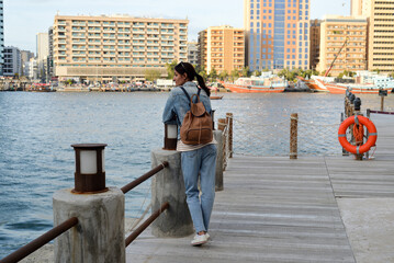 A young woman with a backpack on her back admires the river in the old Dubai Creek. Back view. Journey through the Persian Gulf