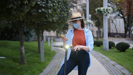 Woman in protective mask with e-scooter and phone on street