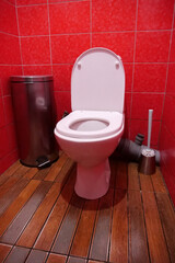 Toilet room with toilet bowl, wastebasket, toilet brush and red wall tiles