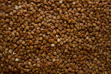 Buckwheat is scattered evenly on the table creating a beautiful background. The texture and shape of buckwheat grains is clearly visible against this background. Pleasant food concept.