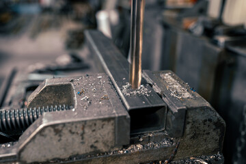 Close-up of a metal bar in a clamp and a drill bit, drilling a hole in a metal rod