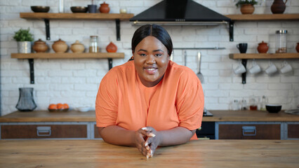 Body positive lady leans elbows on table speaking to camera