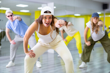 Energetic young girl wearing cap engaging in breakdance in dance studio. Teenagers training Toprock...