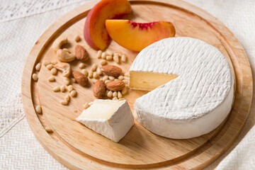 Delicious young homemade Camembert Cheese on a wooden board with peach nuts and slices. Selective focus on a piece of cheese