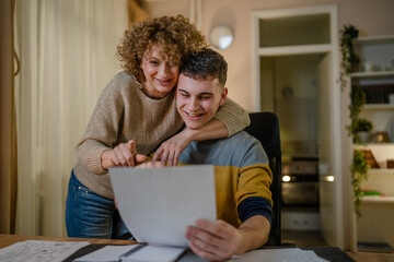 Young man male student teenager and his mother celebrate scholarship read mail letter happy exited...