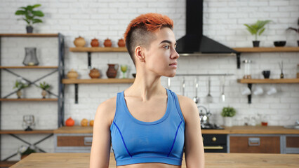 Young woman wearing blue top poses for camera in kitchen