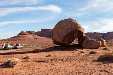 Balanced rock next to a road with a pick up car towing a boat, red desert landscape