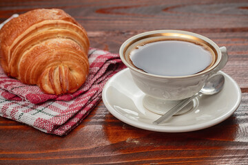 fresh baked croissant and cup of coffee on wooden table.