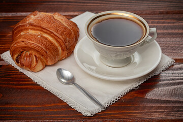 fresh baked croissant and cup of coffee on wooden table.