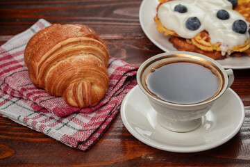 fresh baked croissant and cup of coffee on wooden table.