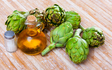 Pile of fresh organic green artichokes with condiments on wooden table