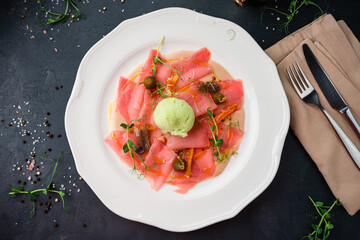 Appetizer of salmon carpaccio with anchovies, capers, sherbet, sauce and microgreens.