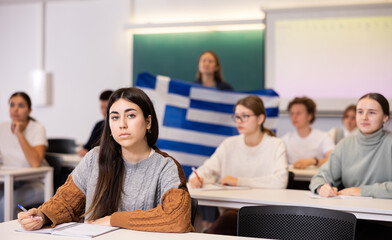 Students study in classroom, teacher stands behind with flag of Greece